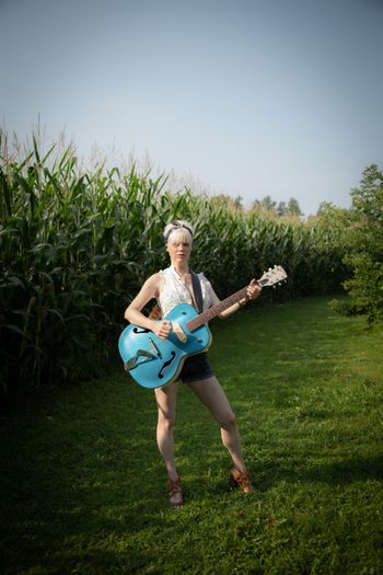 Woman standing outside with a blue guitar.
