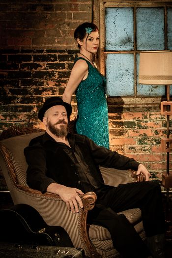 Man seated in an arm chair with woman standing behind him. Indoor setting.
