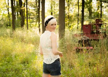 Woman outside in wooded setting looking back at camera.
