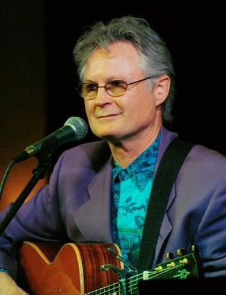 Contact Greg Tamblyn Page: photo of Greg with guitar in front of mic, looking at audience