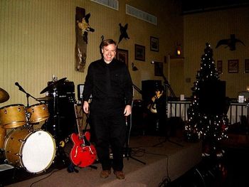 Decoy 12/1/05: Setting up....smilin' Jeff in black pants, black shirt, black tie. To provide a nice backdrop for his Gibson? Hoping to disappear against dark walls? We may never know... [though note 'Joliet' Jake Blues in background is also in black. Also note the killer toppling Christmas tree]
