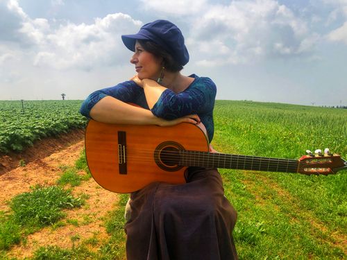 Shira sitting in a field, holding her guitar
