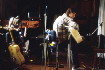 Jeff restrings a guitar in the background as Gary strums in the main studio.
