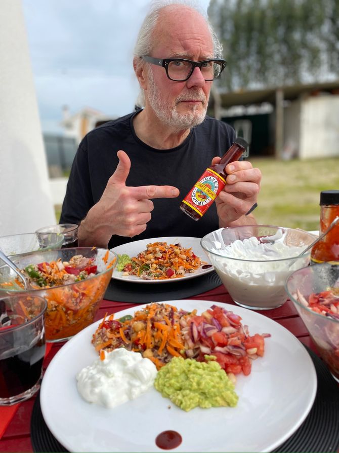 Simon Campbell at home having lunch and holding a bottle of Dave's Insanity Sauce. Photo by Suzy Starlite