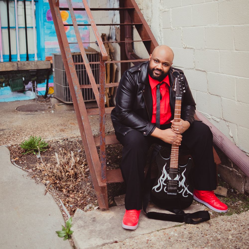 Tory World on stairs in a red an black outfit with a guitar.