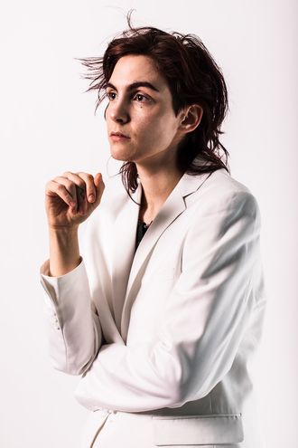 Medusa, trans nonbinary alt-pop musician and rapper; white suit, tuxedo; thoughtful, three quarters profile; photographer Justin Ruggiero