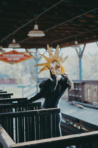 Photo of Medusa at abandoned theme park, wearing Venetian jester mask and clown ruffle collar, reaching out. by Seekaxiom.