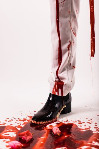 black shoe; teeth along sole; blood dripping down white tuxedo pants; pool of blood on floor; flower petals