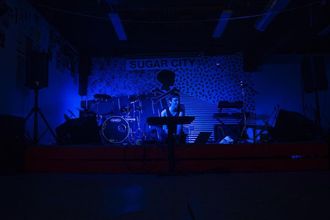 Medusa (pop artist) sitting on the floor of the stage at Sugar City, a DIY venue in Buffalo New York, singing Find Me. The room is dark, lit only by blue light.
