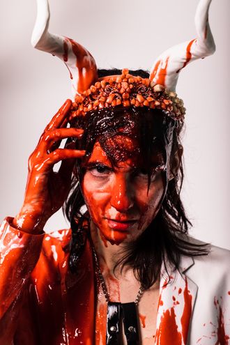 Medusa, trans nonbinary alt-pop musician and rapper; white suit, tuxedo, tiara, horns; bouquet of flowers; fake blood; prom scene, Carrie; photographer Justin Ruggiero