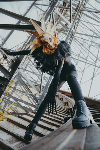 Photo of Medusa, pop musician, at abandoned theme park, removing Venetian jester mask and clown ruffle collar. by Seekaxiom.