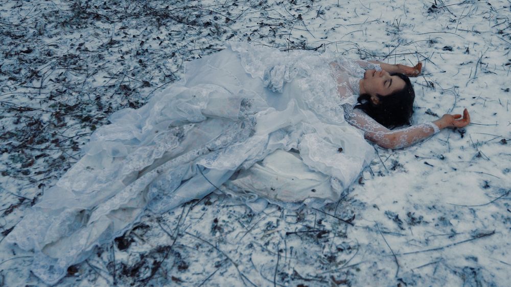 Medusa lies in the dirt and snow, wearing a torn wedding gown,