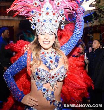 Hire samba dancers like this dancer who’s in a costume covered in silver sequins, red & blue jewels with red feathers on back
