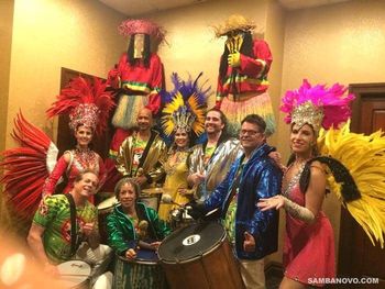 Nine members of the Samba Novo band posing together after a samba show, 3 dancers, 5 drummers and 2 moco jumbies
