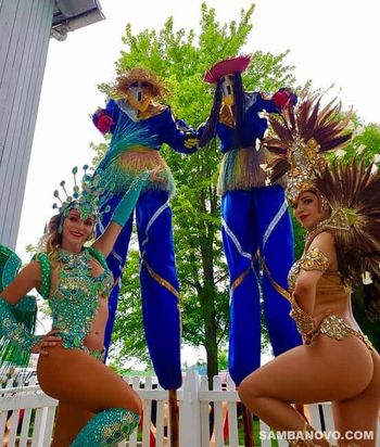 Two beautiful Brazilian samba dancers in featured costumes with green and gold shining sequins posing with two Moco Jumbies
