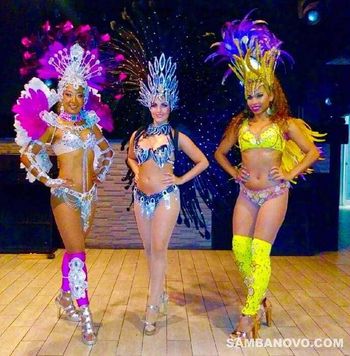 Three dancers of Brazilian samba posing close together in multi-colored costumes made of feathers and glistening sequins
