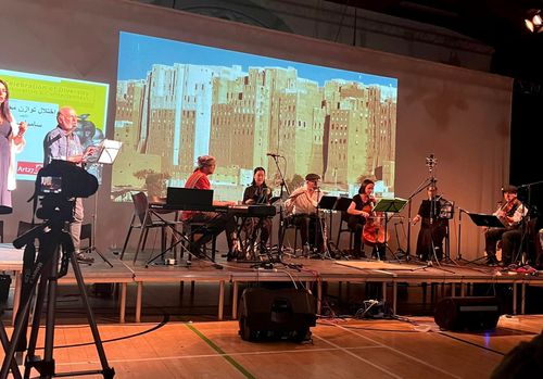 Saber Bamatraf playing his composition Hadhrami Nights with the Southside Symphony at the Festival of Migration, on the screen behind them iconic buildings of Shibam Hadhramout