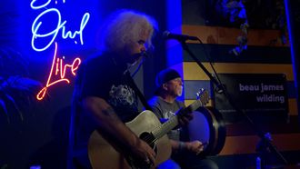 Man with long bleached hair playing guitar next to man playing bodhran.