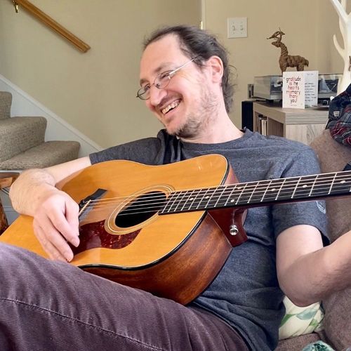 man laughing and smiling while playing guitar on couch