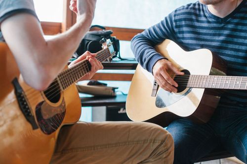 man holding guitar teaching young student also holding guitar