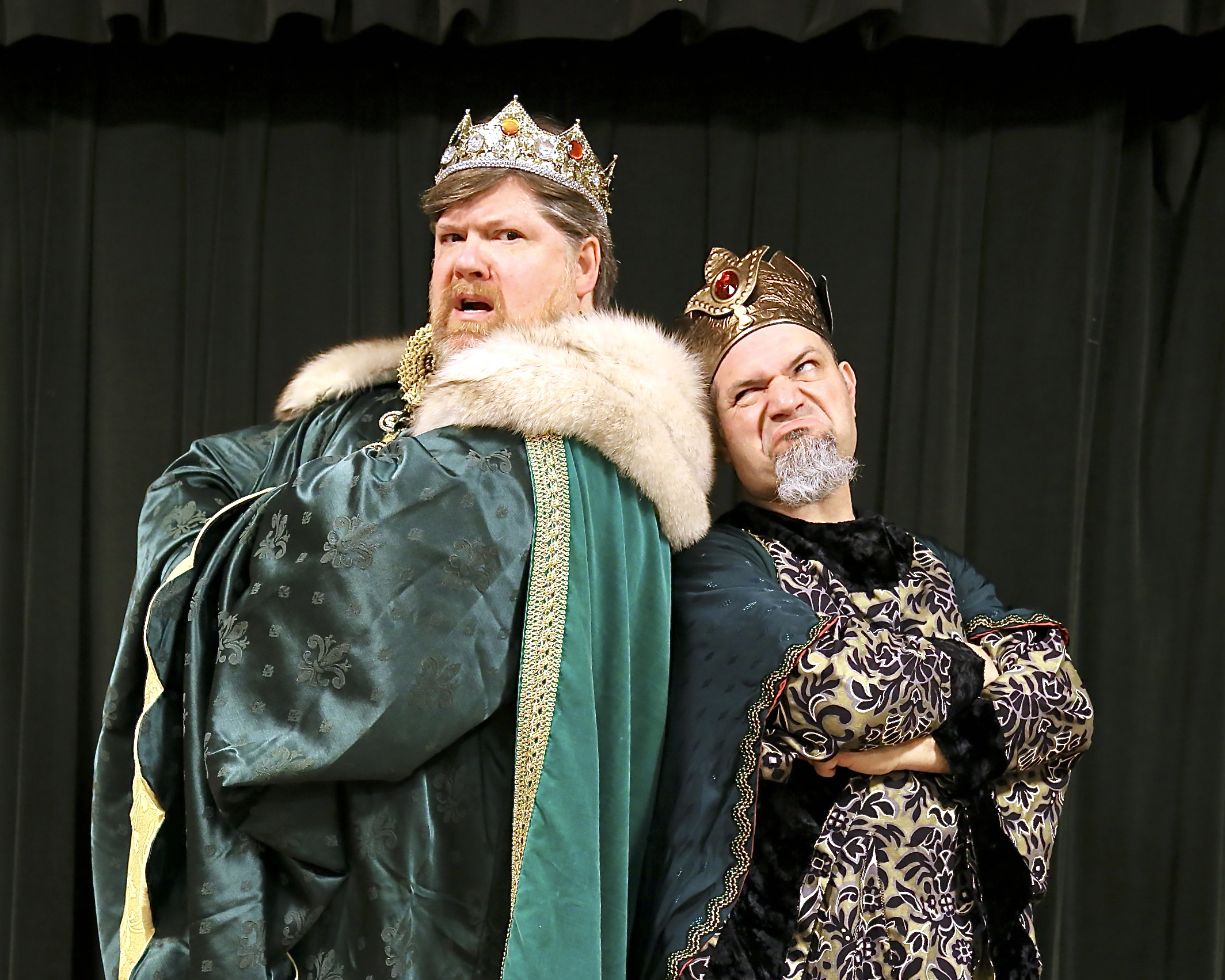 The picture below from Left to Right: Ben Salers (King Hildebrand) and Chris Jurak (King Gama) Dark Curtain Background. King Gama is a red headed and bearded man decked in elaborate emerald green and gold garments with a fur topped cape and gold crown with red jewels. King Gama is grey goateed man in black and gold garments and a dark green cape. He wears a copper crown with 4 large red jewels around. Both stand back to back- looking at each other with particular disgust. 