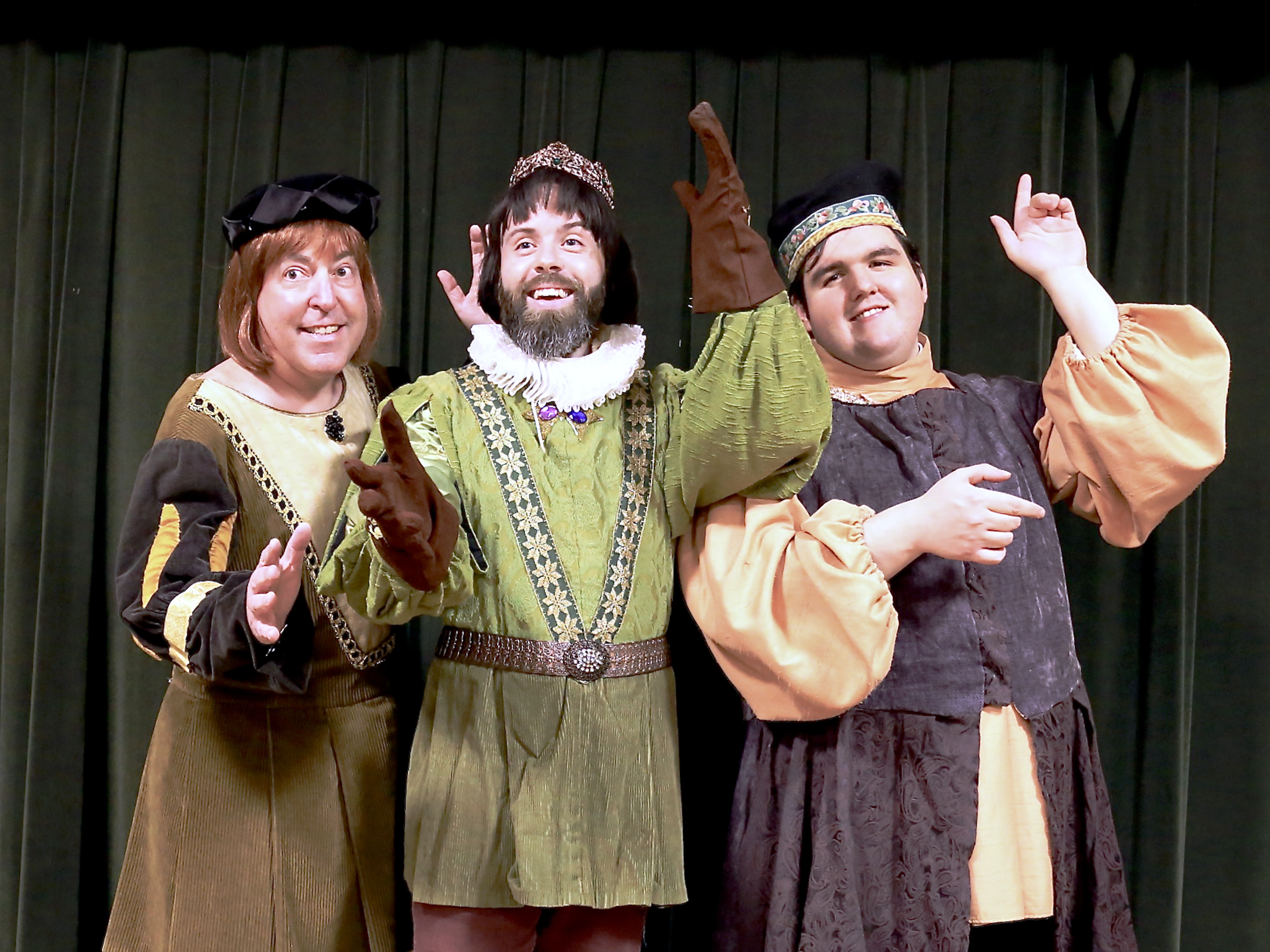 The picture below from Left to Right: Joseph Anthony Smith (Prince Hilarion) and Kara Vertucci (Princess Ida). Dark curtain background. Prince Hilarion, wearing a ruff, green tunic and red pants with matching red gauntlets and a bejeweled bronzish crown, and Princess Ida, wearing a gold necklace, red dress adorned with gold accents, a blue trim, and a black and red academic dress, and atop her head a tall gold crown. Both, crowned, stand back to back wielding swords pointed upright.