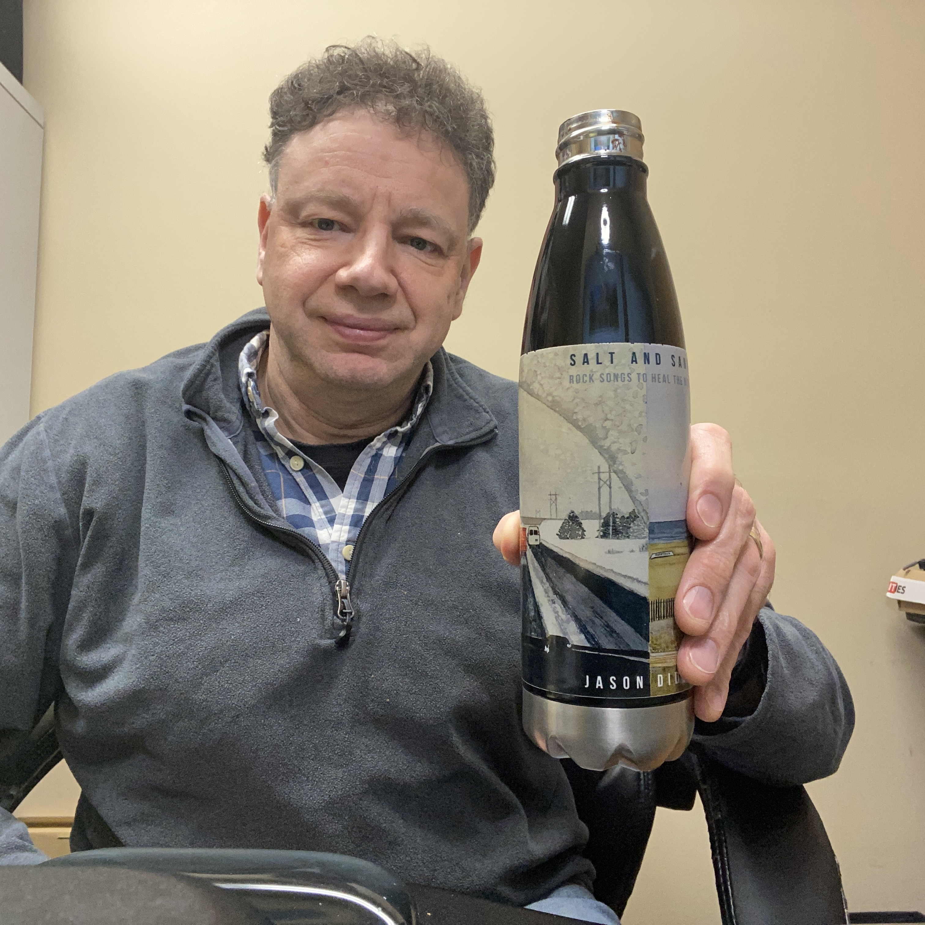 Musician Jason Didner holding a stainless steel water bottle bearing the album artwork for 