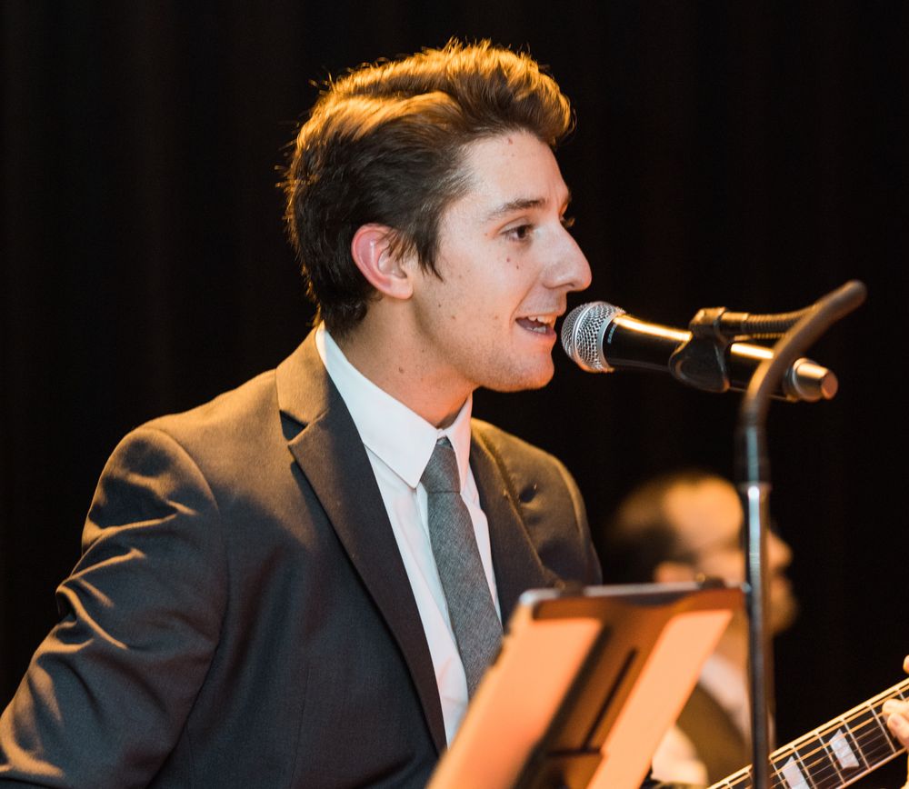 Jake is playing guitar at a wedding in a suit. Photo credit to Pearl Paper Studio.