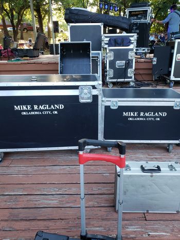 Road cases waiting to be unloaded behind the stage at an outdoor concert.
