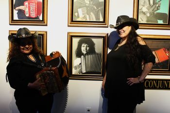 Eva Ybarra and Conjunto Siempre vocalist, Sandy Rodríguez, posing beside her photo at the Tejano Conjunto Hall of Fame and Museum exhibit on display at the San Benito Cultural Heritage Museum. Ybarra is a 2009 inductee. (2022) L – R: Eva Ybarra and Sandy Rodriguez
