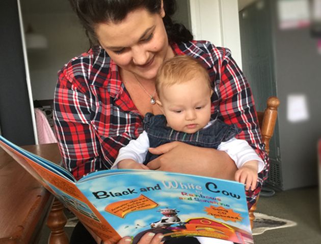 A mum reading the book "Black and White Cow" by Rainbows and Sunshine, to her daughter.