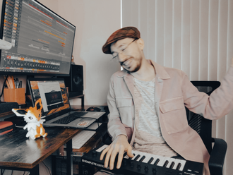 Cataldo Cappiello playfully joking in his home studio while holding a MIDI controller in front of two monitors displaying Cataldo's DAW: Reaper.