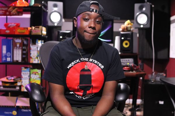 DMV audio engineer Trey Breezy in a black and red WTS Recordings shirt sitting in front of a desk with audio engineering equipment on it and a shelf full of candy.