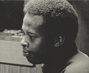 A young David Porter is shown while composing in the studio with Isaac Hayes at a creative pensive point. The picture also shows a view of the control room window of Stax Records’ Studio A.
