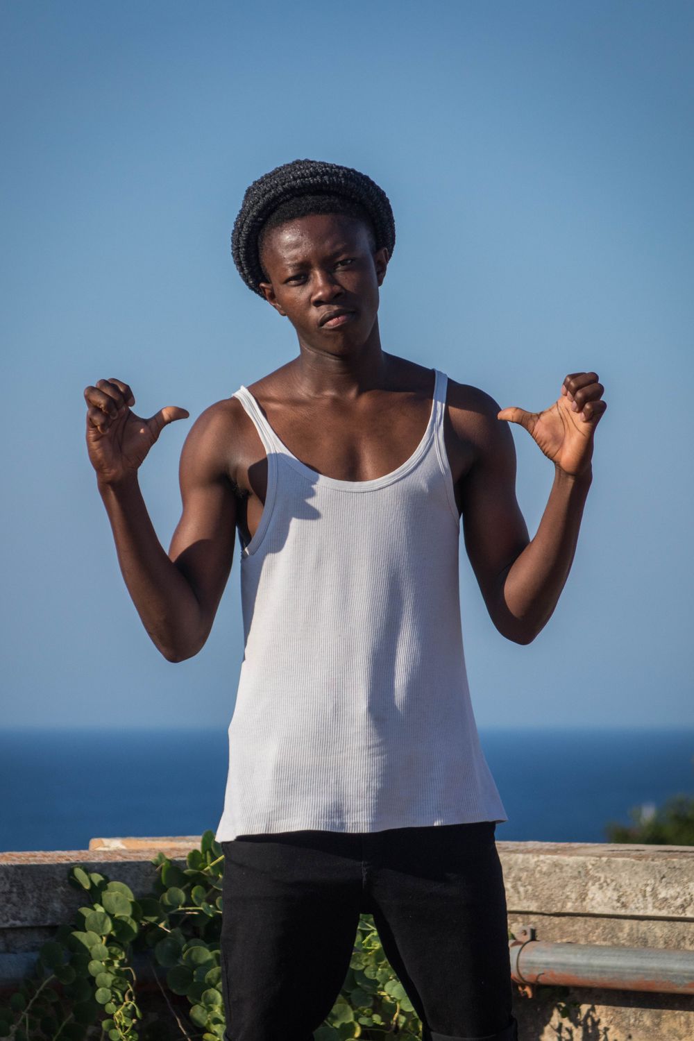 Austin – June 2017, Syracuse, Sicily. Austin, a 17-year-old Nigerian migrant, strikes a pose on the rooftop terrace of Umberto Primo. The Mediterranean Sea, which he bravely crossed, is in the background. Austin was a passionate dancer at the camp music sessions and concerts. 