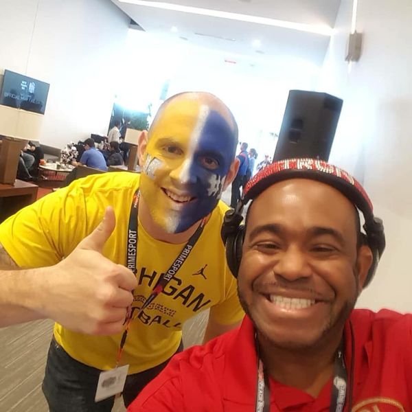 DJ Tron posing with a University of Michigan Fan with his face painted blue and yellow