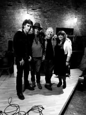 A black and white photo of four people standing with arms around each other's shoulders.  On the left is a tall man in black with an Elvis-type pompadour (Michael Ubaldini).  Next to him is a man in a hat with a bandanna around his neck (Mark Huff).  We are to the right of both of them, smiling.  Ron is wearing cuffed jeans and Jen is in a black dress and light colored sweater.