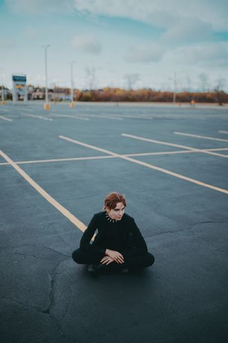 Medusa, non-binary trans pop hip-hop musician, sitting in parking lot, legs crossed. photo by seek axiom.