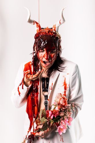 Medusa, trans nonbinary alt-pop musician and rapper; white suit, tuxedo, tiara, horns; bouquet of flowers; fake blood; prom scene, Carrie; photographer Justin Ruggiero