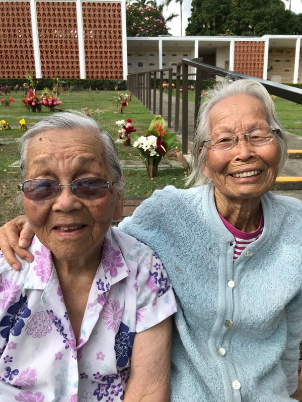 Summer 2018: Betty Mieko Mente Toyama with younger sister Thelma Fumiye Mente Kobayashi (d. 12-3-2021). They are at Nuuanu Memorial Park cemetery. Notice the flowers in between their heads. That is the location of the “Mente” family grave.