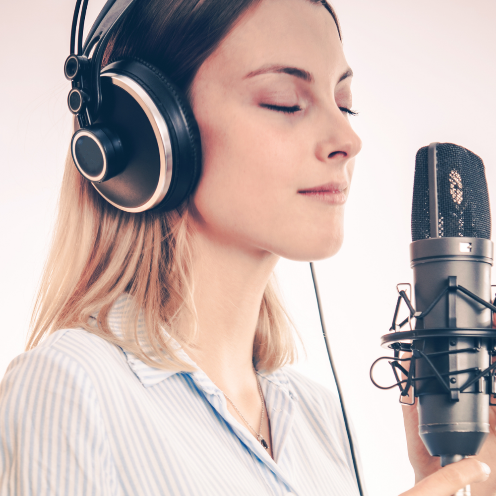 Woman standing close to a vocal microphone in a relaxing state with earphones on her ears.