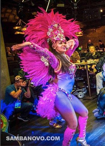 Hire Brazilian dancers for your birthday party or any event. This dancer is in a purple & pink costume performing at a party
