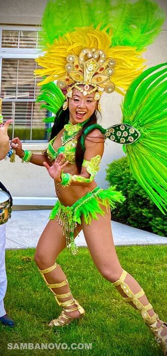 Choose a Brazilian dancer for a birthday party like this dancer who has a big smile wearing a bright green feathered costume
