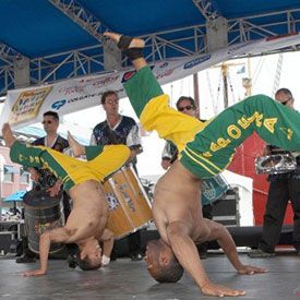 Two Brazilian Capoeria performers on stage with samba drummers playing behind them