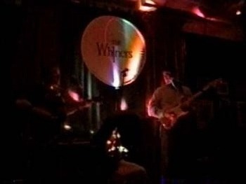 Whiners band on stage with Whiners written on a cirlce screen in back of stage
