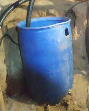 Photo of blue barrel with black hose and dirt