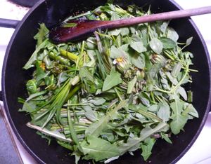 Photo of cast iron fry pan with edible wild greens and wooden spoon