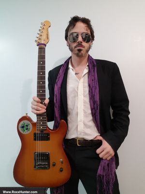 Guy in suit, with purple scarf holding guitar wearing shades!